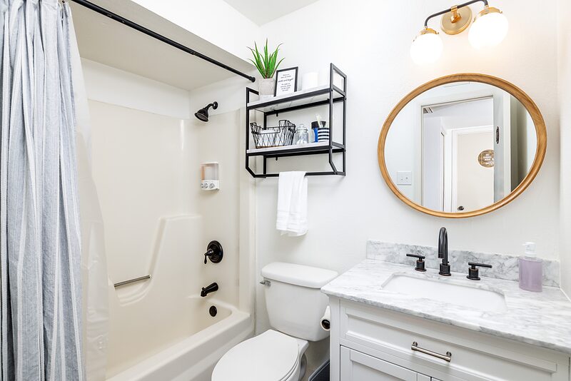 Bathroom with a shower tub combination, round mirror, and marble vanity
