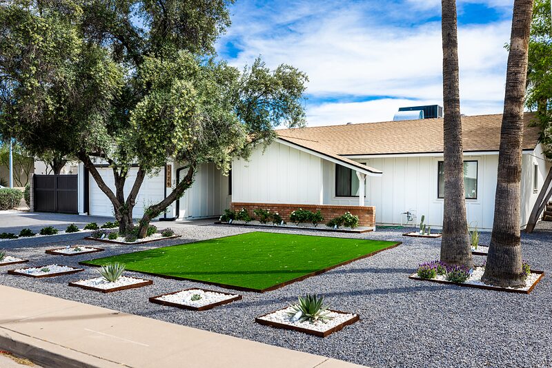 Front of the house with a turf lawn, gravel beds, and mature palms