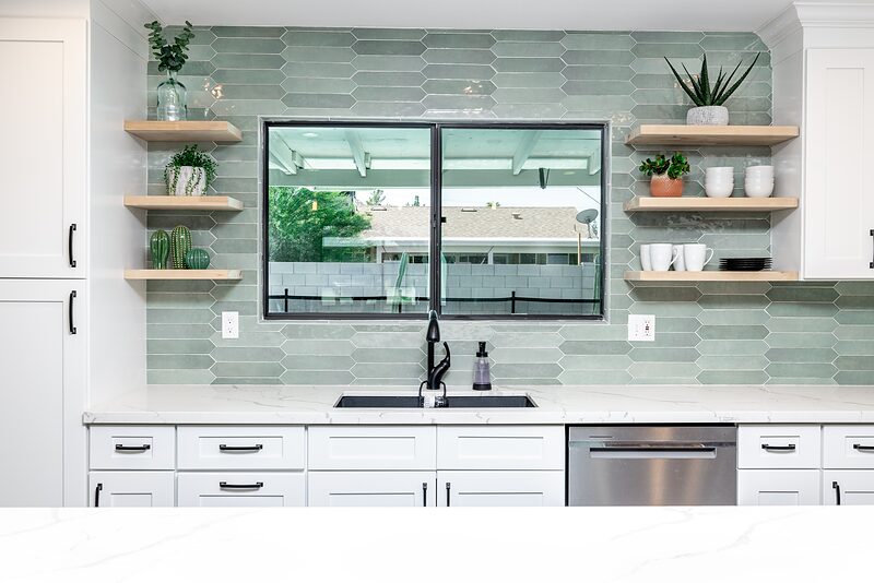 Kitchen sink under a window with green tile backsplash and open shelving