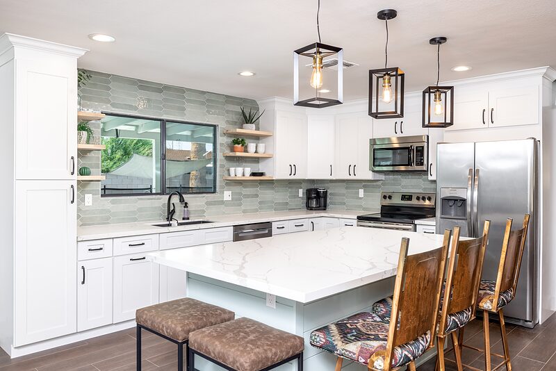 White kitchen with a quartz island, pendant lights, and stainless appliances
