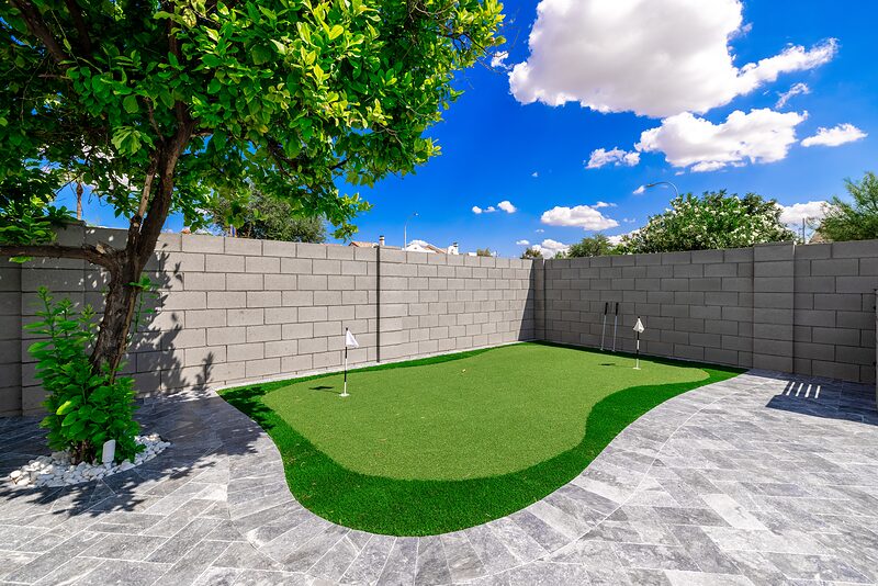 Artificial turf putting green with flags, shaded by a citrus tree
